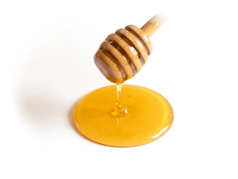 Honey falling from a wooden dipper into a small golden pool